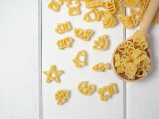 raw children's pasta in the form of different animals, stars and bells on a wooden spoon