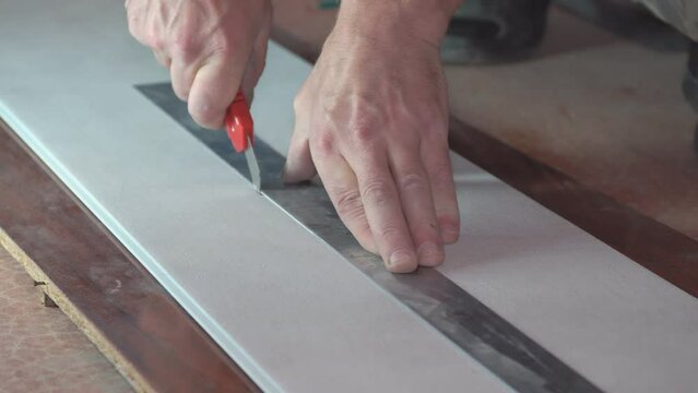 A man cuts a plastic pvc panel with a construction knife