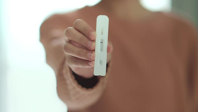 Woman looking at test and showing negative results on test strip, Coronavirus pandemic protection. Female using rapid antigen test kit for self test covid-19 epidemic at home.