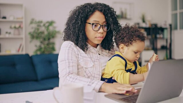Black business woman doing her job on laptop and babysitting with little son