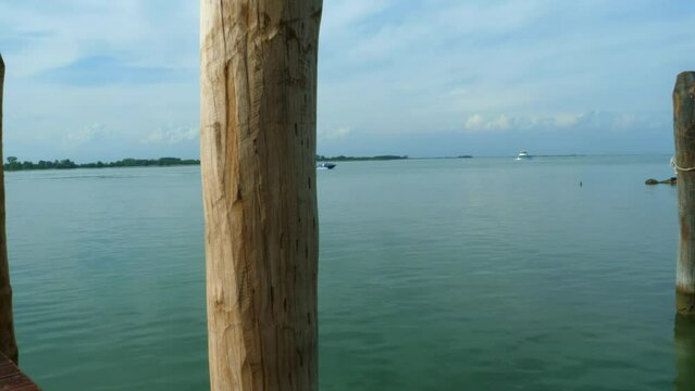 beautiful jetty in Italy, Venice, on the blue green sea with two boats passing by with a pole in the centrum all in all a a beautiful sunny summer day with blue clouds pan