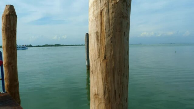 beautiful jetty in Italy, Venice, on the blue green sea with a boat passing by with a pole in the centrum all in all a a beautiful sunny summer day with blue clouds frame