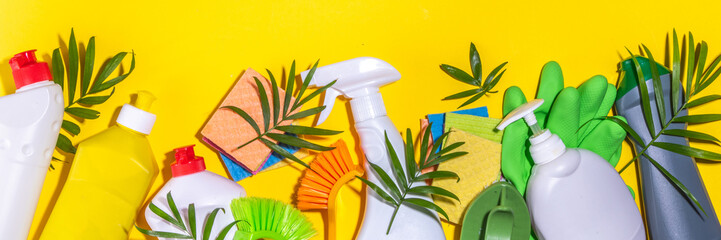 Summer cleaning concept. Plastic basket with different detergents and cleaning supplies bottles, accessories for cleaning house with palm leaves on a bright yellow background