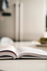 Open hardcover book with white pages lies on artificial stone table at kitchen, fridge on background. Books spine. Selective focus. Vertical stories background.