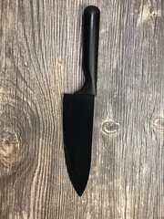The black knife lying on the table with wooden texture. Close up image of the black knife on the wooden background.