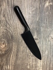 The black knife lying on the table with wooden texture. Close up image of the black knife on the wooden background.