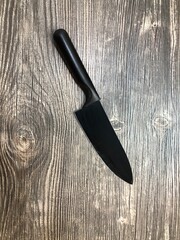 The black knife lying on the table with wooden texture.
Close up image of the black knife on the wooden background.