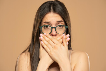 Ashamed woman with hand over mouth on a beige background