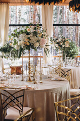 Wedding. Banquet. Decor. Festive tables on the terrace in the forest are decorated with compositions of white flowers and greenery, there are candles, plates with numbers, plates and glasses