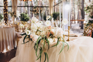 Wedding. Banquet. Decor. Festive tables on the terrace in the forest are decorated with compositions of white flowers and greenery, there are candles, plates with numbers, plates and glasses