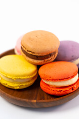 Multicolored macarons on a wooden plate on a white background.
