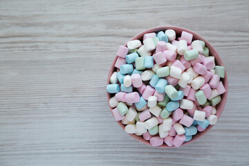 Rainbow Fruity Mini Marshmallows in a Pink Bowl on a white wooden background, top view. Flat lay, overhead, from above. Copy space.