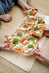  hands taking slices of slice of pizza into wooden table