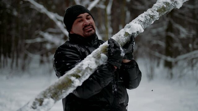 strong man is lifting log in winter forest, training alone in nature, keeping fit