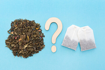 Choice between loose leaf green tea and tea bags. Wooden question mark. Blue background. Dried...