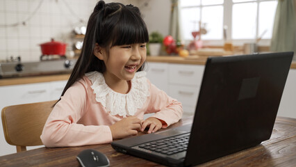 cute smiling asian girl talking happily with friends and have group classes through online video conferencing technology on laptop computer at dining table in bright home interior.