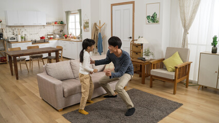Full length of cheerful Asian family of three father, mother and daughter relaxing dancing to music in a modern bright home interior.