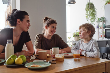 Happy lesbian couple talking to adopted child while having breakfast at table at home