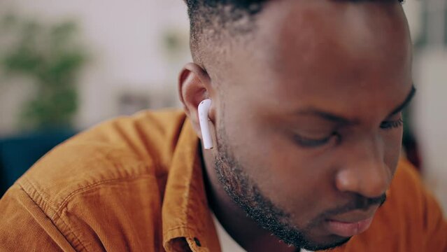 Black man using wireless earbuds while having online video call, modern tech