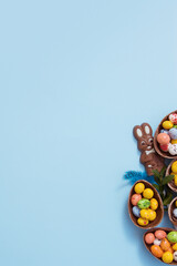 Fototapeta na wymiar Flat lay Easter hunt concept with chocolate eggs and bunny on blue background. View from above