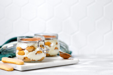 Two glass jars with lid with tiramisu  dessert. Cake with cream, italian dessert. Marble board, sunshine. Copy space.