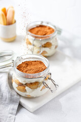 Pouring cocoa to tiramisu dessert. Traditional Italian dessert tiramisu in jars.  Dessert made with savoiardi and cream decorated with cocoa powder.