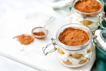 Traditional tiramisu dessert in jars.  Dessert made with savoiardi and cream, decorated with cocoa powder.