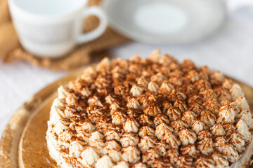 Homemade tiramisu cake with cocoa on top on wooden platter on white tablecloth