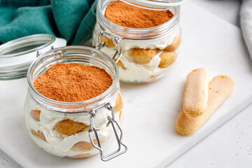 Tiramisu dessert with glass jars with a lid on a marble board and a gray background, green napkin....