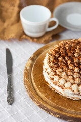 Homemade tiramisu cake with cocoa on top on wooden platter on white tablecloth