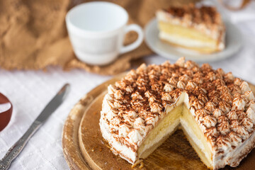 Homemade tiramisu cake with cocoa on top on wooden platter on white tablecloth