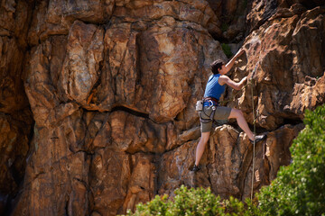 Fototapeta premium Hanging on tightly. A wide shot of a young woman rock climbing.
