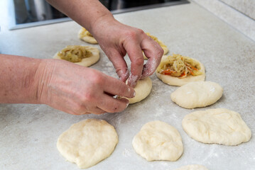hands of  female cook put the stuffing in the pies. cabbage pies are ready to be cooked in frying pan