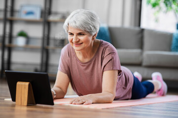 sport, fitness and healthy lifestyle concept - smiling senior woman with tablet pc computer exercising on mat at home