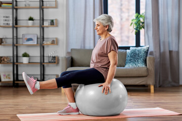 sport, fitness and healthy lifestyle concept - smiling senior woman training by sitting on exercise...