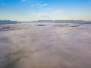 Fototapeta na wymiar Flight over fog in Ukrainian Carpathians in summer. A thick layer of fog covers the mountains with a solid carpet. Mountains on the horizon. Aerial drone view.