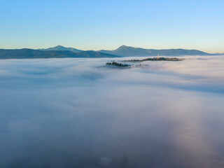 Sunny morning in the foggy Carpathians. A thick layer of fog covers the mountains. Aerial drone view.