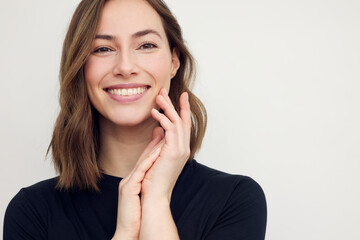 Portrait of young smiling woman looking happy on white background. Big smile on her face, looking beautiful and cute with hands touching her cheek.	