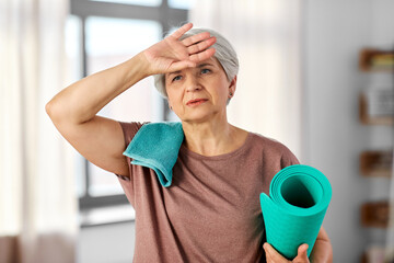 sport, fitness and healthy lifestyle concept - tired senior woman with yoga mat and towel at home