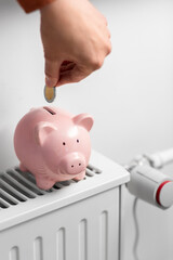 heating, energy crisis and consumption concept -close up of hand putting coin into piggy bank on...