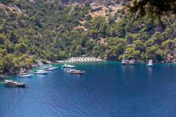 Fototapeta na wymiar Amazing aerial view of Butterfly Valley in Fethiye Turkey. Summer landscape with mountains, green forest, azure water, sandy beach and blue sky in bright sunny day. Travel background. Top view. Nature