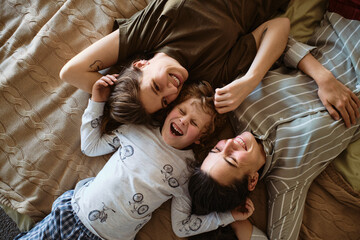 High angle view of happy lesbian family lying on bed with their son and laughing