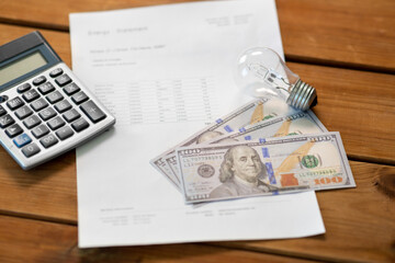 Obraz premium electricity, energy crisis and power consumption concept - close up of utility bill, calculator, money and lightbulb on wooden table