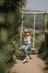 Thai woman in casual style is sitting on swing in an orange garden