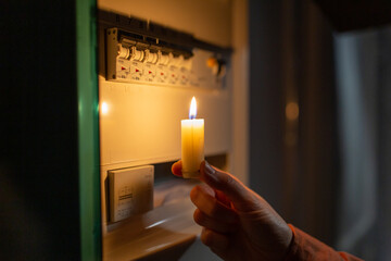 electricity, energy crisis and power consumption concept - close up of hand holding burning candle...
