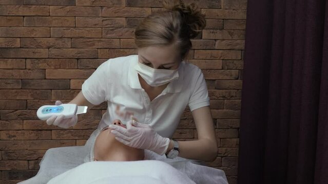 Woman receives youth and skin care procedure. Cosmetologist cleans female face with hardware technique. Ultrasonic face cleaning in a beauty salon