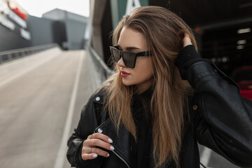 Urban female portrait of a beautiful stylish hipster girl in a trendy black leather jacket and...
