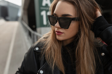 Street female portrait of young pretty woman with fashion sunglasses in black leather jacket walks in the city