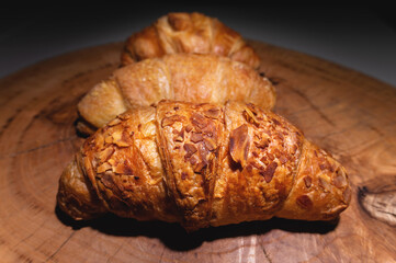 Close-up of a pile of three croissants on a wooden board against a dark background. Delicious and healthy breakfast