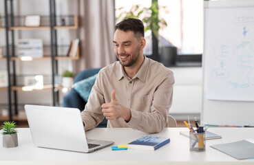 Fototapeta premium distance education, school and remote job concept - happy smiling male teacher with laptop computer having online class at home office showing thumbs up